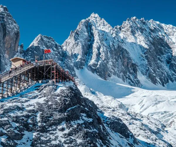 Yulong snow Mountain,Lijiang,Chinatravel Wooden viewing platform on a snowy rocky ridge with a red flag, set against towering snowy mountains.