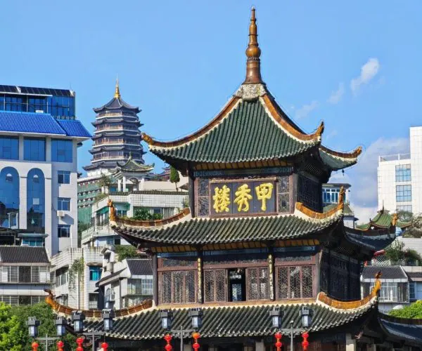 Jiaxiu Tower,Guiyang,Chinatrip Traditional Chinese pavilion with curved green tiles and gold sign, set against modern buildings; visitors walk along a stone walkway under red lanterns.