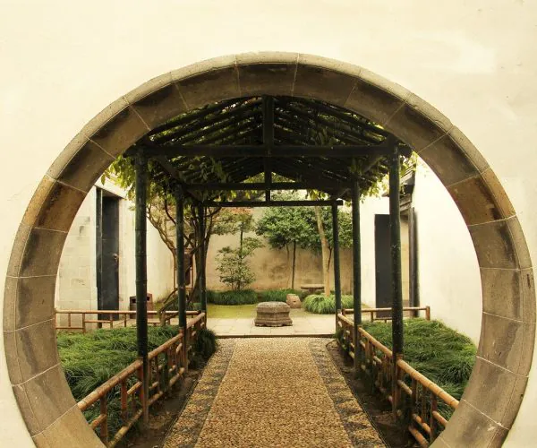 Lingering Garden,Suzhou,Chinatravel Circular stone gate framing a stone path through a tranquil garden courtyard with greenery on both sides.