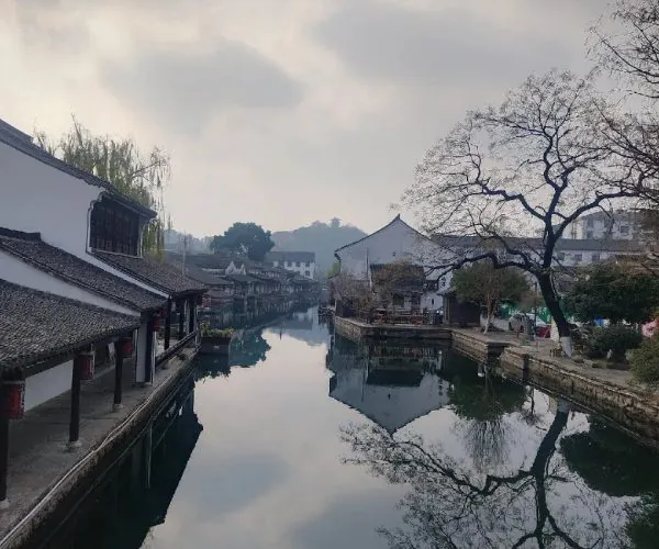 Calm canal in a historic town with white-walled buildings and tiled roofs, mirrored in the water.