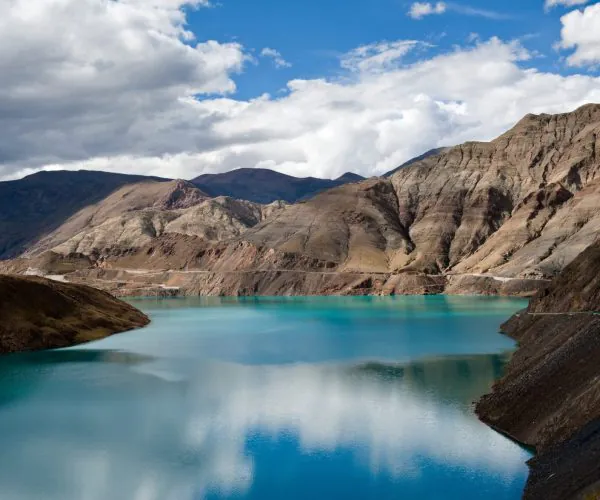 Yamdrok Lake,Lhasa,Chinatravel Turquoise lake nestled among rugged brown mountains under a partly cloudy blue sky.