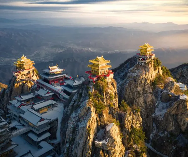 Laojun Mountain,Luoyang,Chinatravel A dramatic mountain temple complex with yellow pagodas perched on rocky cliffs at sunset, red railings guiding the path between buildings.