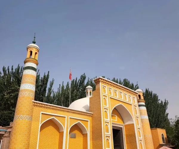 Id Kah Mosque,Kashgat,China tour Yellow brick mosque gateway with tall minarets, arched entrance, and decorative white patterns against a clear blue sky, steps leading up to the door