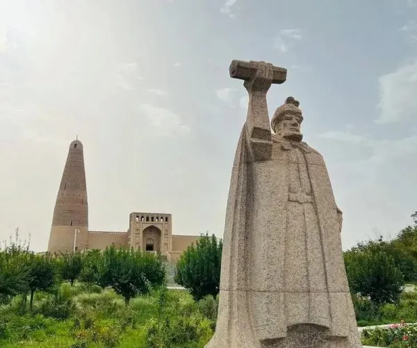 Sugong Pagoda,Turpan,China tour Statue of a man in robes raising a hammer, in a garden with a tall monument and arched building in the background, under a blue sky.—Informative image with surrounding structures visible.