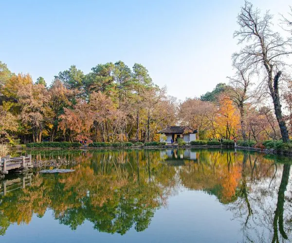 Suzhou Weather,Suzhou,Chinatravel Autumn park scene with a calm pond, colorful trees, and a small pavilion reflected in the water. a wooden walkway extends over the pond on the left.