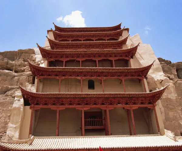 Mogao Caves (UNESCO World Heritage),Dunhuang,Chinatrip Five-story red Chinese pagoda built into a rocky cliff under a blue sky, with carved wooden eaves and balconies alternating as it rises above the rock face.