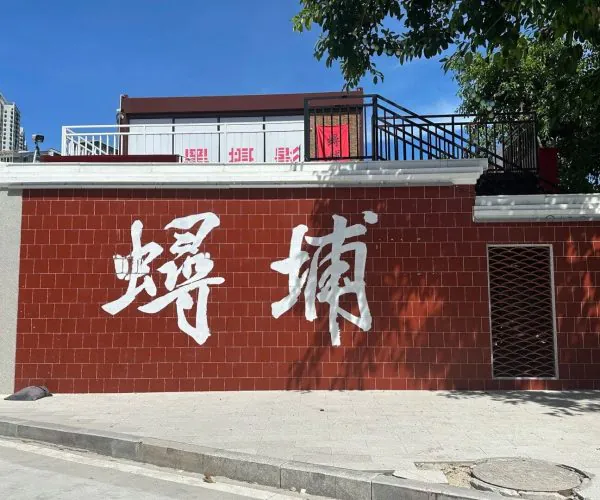 Xunpu Village,Quanzhou,Chinatravel Large white Chinese characters painted on a red tiled wall under a clear blue sky, with a tree casting shadows nearby.