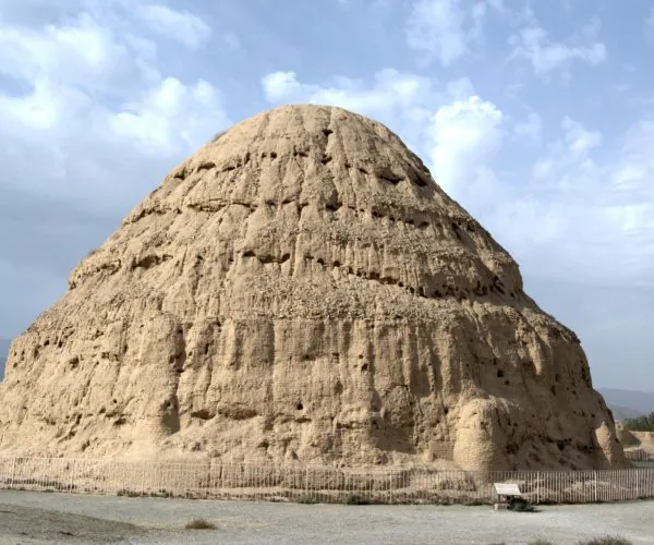 Western Xia Imperial Tombs,Yinchuan,Chinatrip Large rounded earthen mound with vertical grooves, surrounded by a low fence in a desert setting.