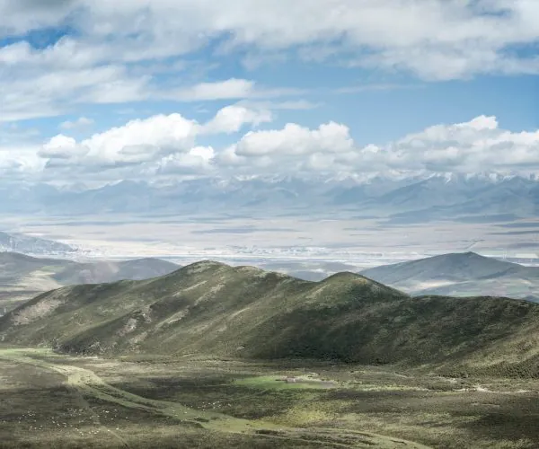 Xining Weather,Xining,Chinatrip Wide valley with rolling green hills in the foreground, and distant snow‑capped mountains under a blue sky with clouds.