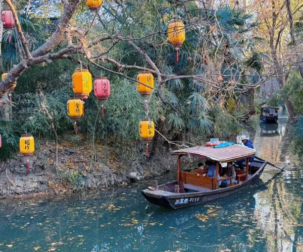 Xixi National Wetland Park,Hangzhou,Chinatravel Wooden passenger boat cruising a narrow canal, lanterns strung in trees above and autumn leaves floating on the water.