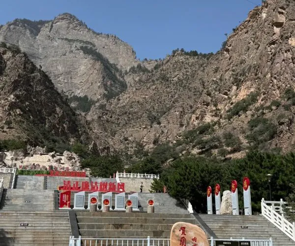 Helan Mountain National Forest Park,Yinchuan,Chinatrip Stone monument in a plaza at the base of rugged mountains, with red banners and a set of wide steps leading up to the entrance area.