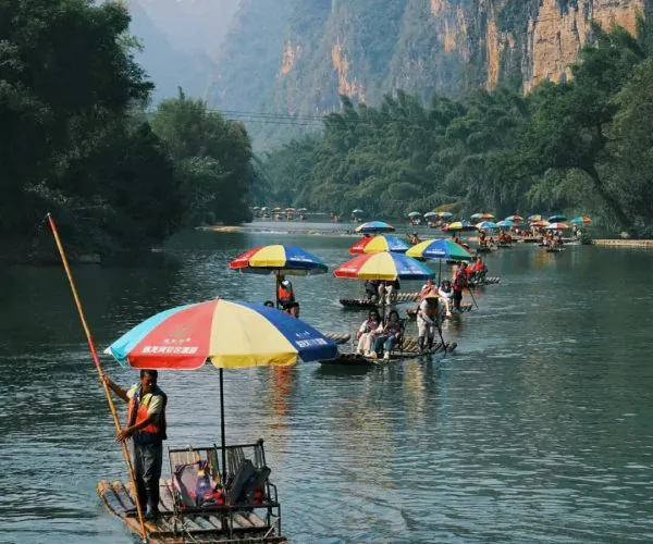 Yulong River Bamboo Rafting,Yangshuo,Chinatravel Bamboo rafts with colorful umbrellas drift along a calm river framed by towering karst cliffs and green trees.