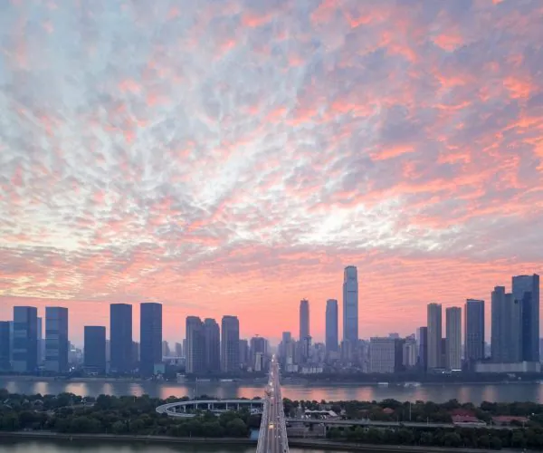 Changsha Weather,Changsha,Chinatravel Sunset sky with pink clouds over a city skyline and a long bridge crossing a river in the foreground.”,