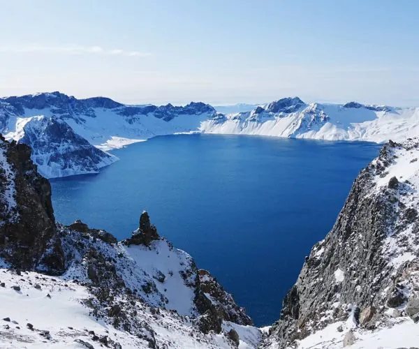 Baishan North Slope Scenic Area,Baishan,Chinatrip Snow-covered mountains surround a deep blue lake, viewed from a snowy ridge under a clear sky, high in the mountains.