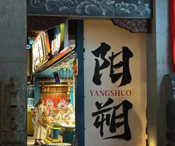 Yangshuo Town Historic Streets,Yangshuo,Chinatravel Storefront of a Chinese restaurant with large black calligraphy and 'YANGSHUO' on the wall; interior counter with customers selecting food.