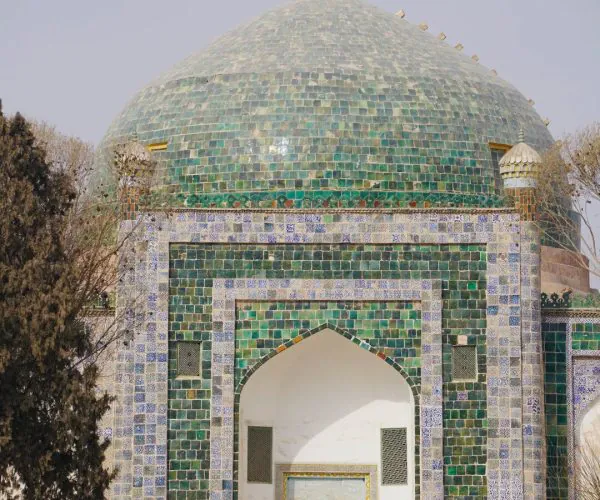 Abakh Hoja Tomb,Kashgar, China tour Teal-green tiled Islamic dome building with an arched entrance and visitors entering the doorway.