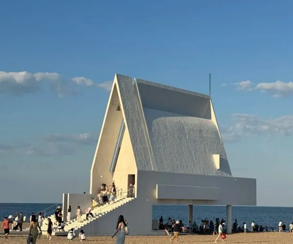Aranya Community,Qinhuangdao,Chinatravel White modern chapel on a beach with a wide staircase and visitors gathered around the entrance.