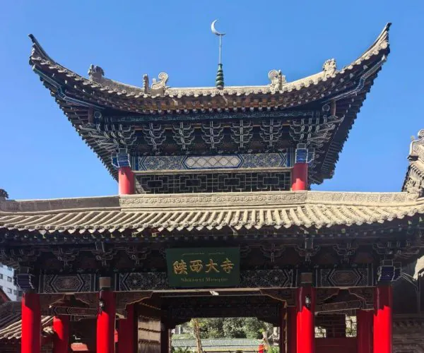 Shaanxi Mosque,Urumqi,Chinatrip Entrance gate to a traditional Chinese temple with ornate tiled roof, red pillars, and a decorative green signboard above the passageway.