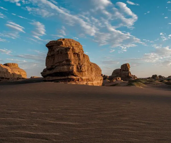 Yardang National Geopark,Dunhuang,Chinatrip Desert landscape with large sandstone rock formations rising from flat sandy dunes under a blue sky with wispy clouds.