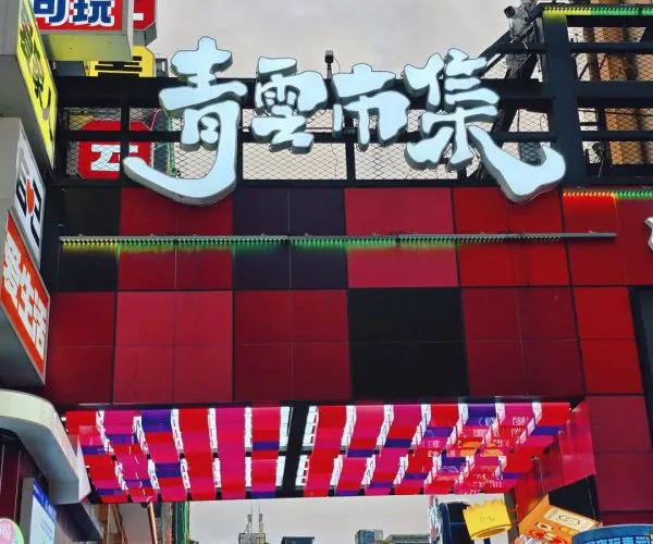 Qingyun Market,Guiyang,Chinatrip Busy urban shopping street with a large white, stylized Chinese sign over a red storefront arch, surrounded by colorful neon signs and banners in Chinese.