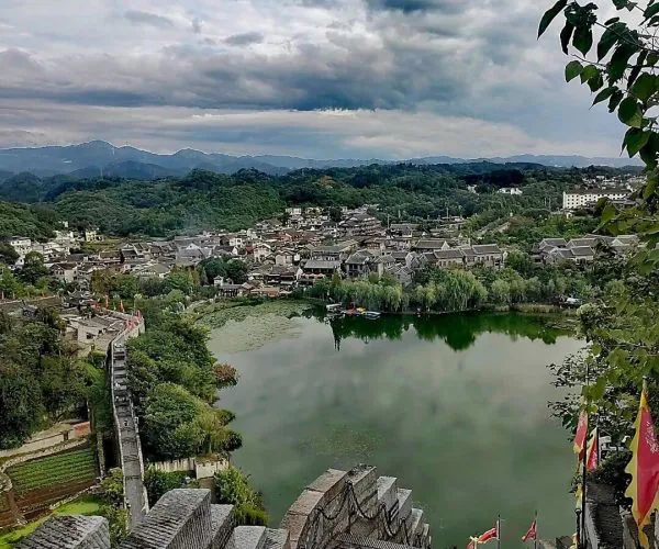 Qingyan Ancient Town,Guiyang,Chinatrip Stone stairway leads down to a green lake in a historic town nestled among hills and cloudy skies above