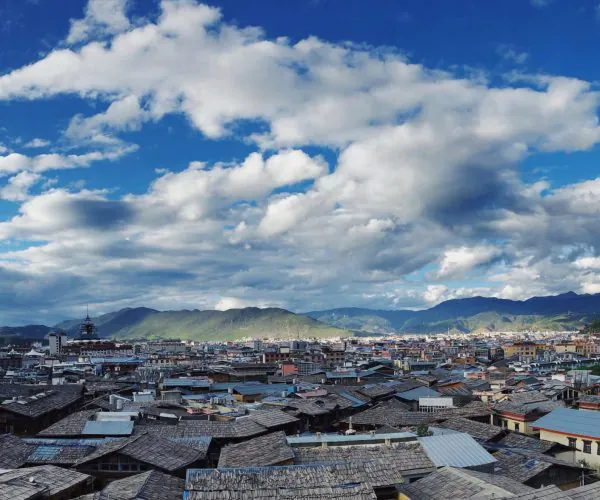 Shangri-La,Yunan,Chinatravel Cityscape with dense rooftops in the foreground, green hills in the distance, and a blue sky with scattered clouds.