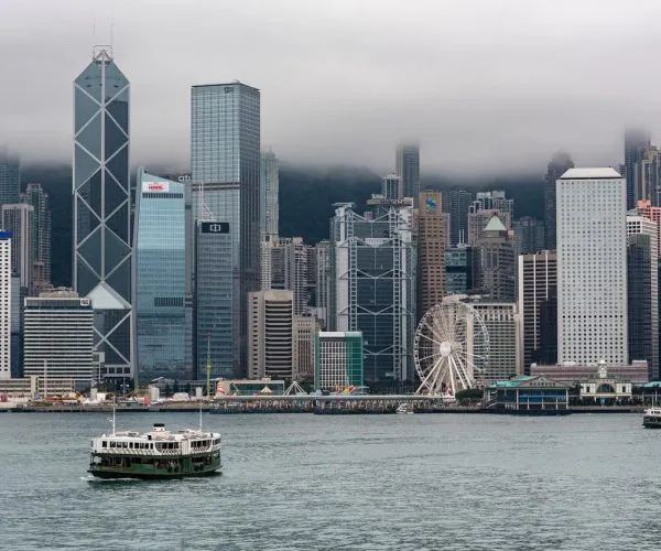Hongkong,Guangdong,Chinatravel City skyline along the water with a ferris wheel and tall glass skyscrapers; a ferry boat on the foreground harbor.