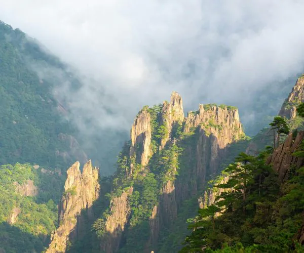 Yellow Mountains ,Huangshan,Chinatravel Jagged rocky mountain peaks with green trees and low-hanging clouds in a misty valley.