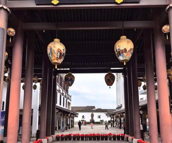 Yellow Wine Town,Shaoxing,Chinatravel Entrance to a traditional Chinese street with red-capped pots lined along a stone path and hanging lanterns under a dark wooden signboard with gold characters.