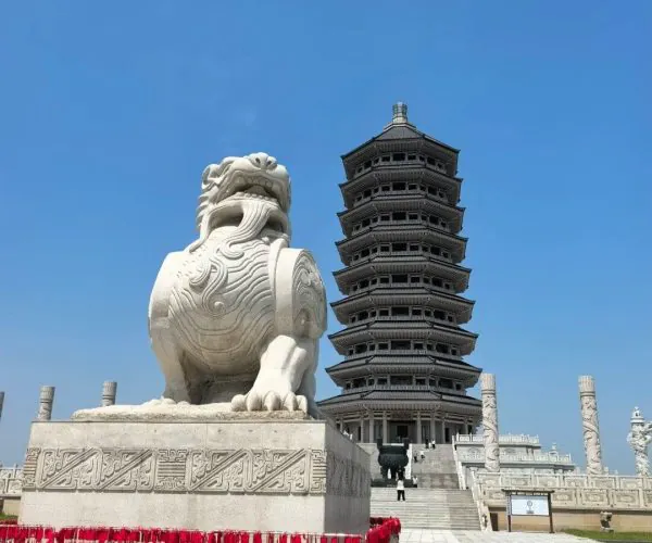 Heixiazi Island Tourist Area,Jiamusi,Chinatravel Large white stone guardian lion statue in front of a multi-tiered pagoda under a clear blue sky.