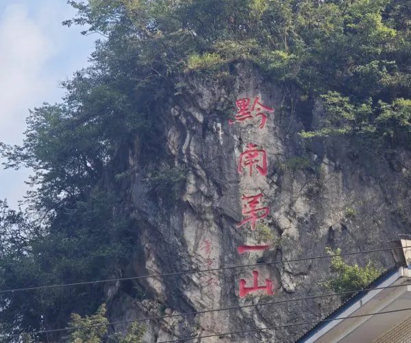 Qianling Mountain Park,Guiyang,Chinatrip Rock cliff with large red Chinese characters painted vertically, greenery above and a building roof at the base in the foreground.